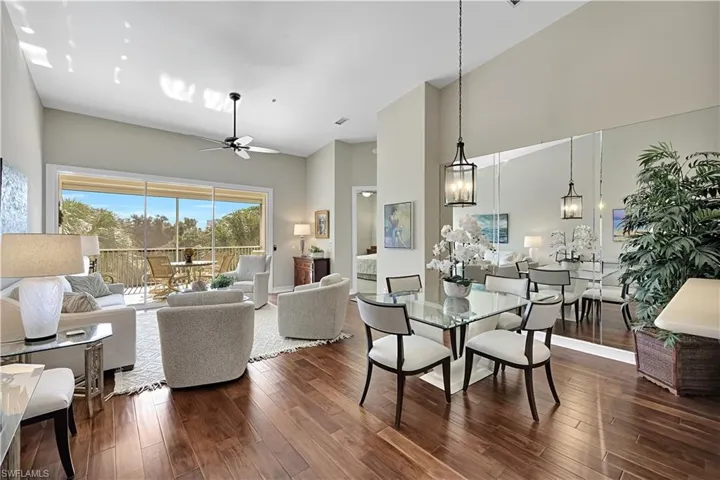 Open-concept interior featuring high vaulted ceilings, wood-finish flooring, sliding glass doors, full-wall mirrored accents, and a pendant lantern light fixture