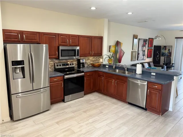 Kitchen with stainless steel appliances, dark countertops, wood finish floors, a peninsula, and decorative backsplash