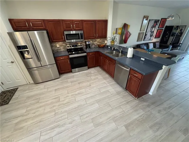 Kitchen with dark countertops, stainless steel appliances, a peninsula, open floor plan, and wood tiled floors