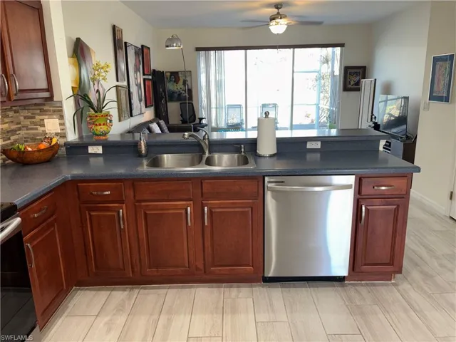 Kitchen featuring open floor plan, stainless steel dishwasher, electric range oven, dark countertops, and light wood-type flooring
