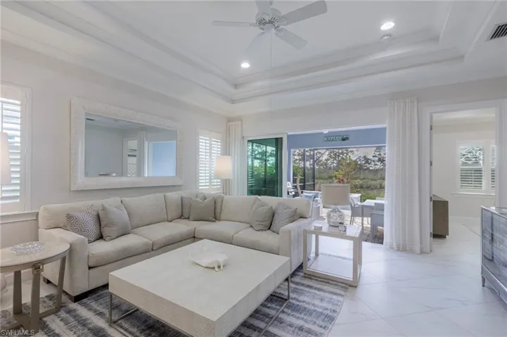 Living room with a raised ceiling, ceiling fan, plenty of natural light, and ornamental molding