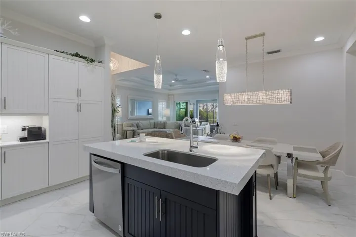 Kitchen featuring white cabinets, sink, a center island with sink, dishwasher, and hanging light fixtures