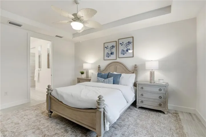 Bedroom featuring a tray ceiling, light wood-style floors, ceiling fan, and ensuite bathroom