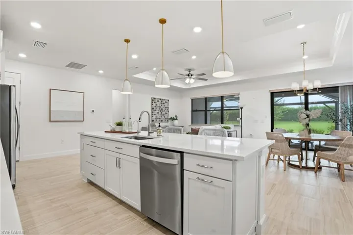 Kitchen featuring a raised ceiling, white cabinetry, decorative light fixtures, ceiling fan, and stainless steel appliances