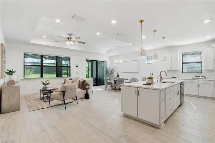 Kitchen with open floor plan, a tray ceiling, decorative light fixtures, white cabinetry, and a center island with sink