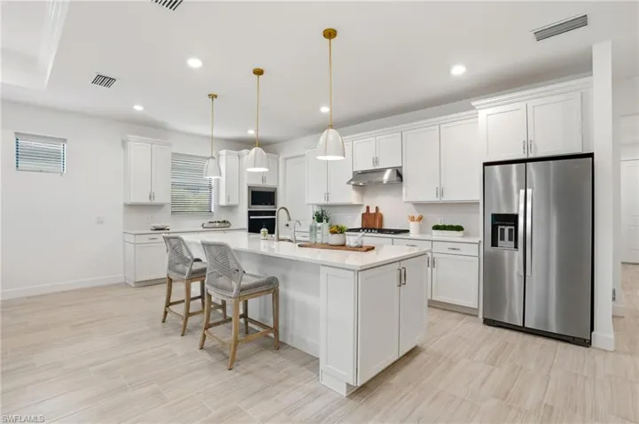 Kitchen featuring appliances with stainless steel finishes, a kitchen bar, tasteful backsplash, decorative light fixtures, and a kitchen island with sink