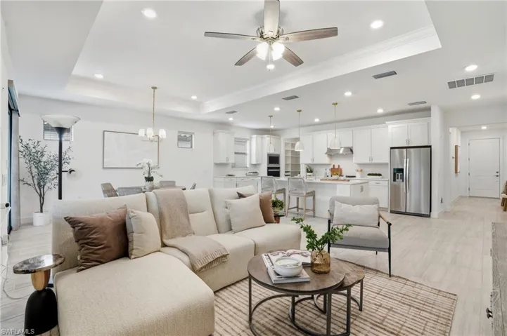 Living area featuring a tray ceiling, a chandelier, light wood-type flooring, recessed lighting, and ceiling fan