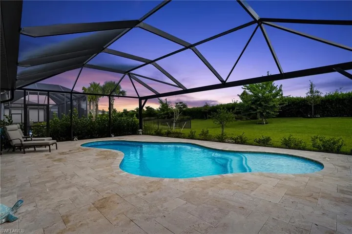 Pool at dusk featuring a sunroom, an outdoor pool, a lanai, and a lawn