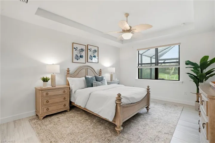 Bedroom with a tray ceiling, ceiling fan, and light wood-style floors