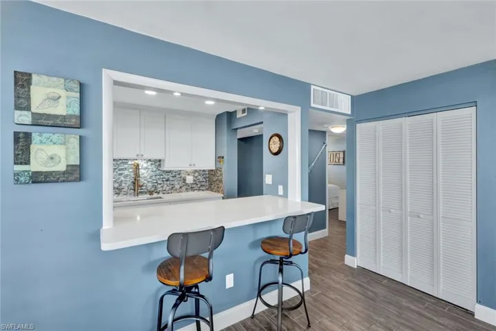 Kitchen featuring white cabinetry, tasteful backsplash, a kitchen breakfast bar, a peninsula, and dark wood finished floors