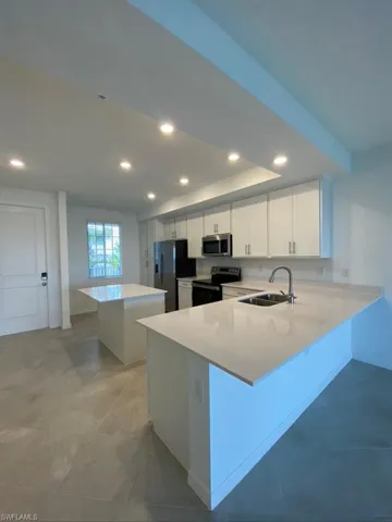 Kitchen with a center island, a kitchen breakfast bar, recessed lighting, white cabinetry, and a peninsula