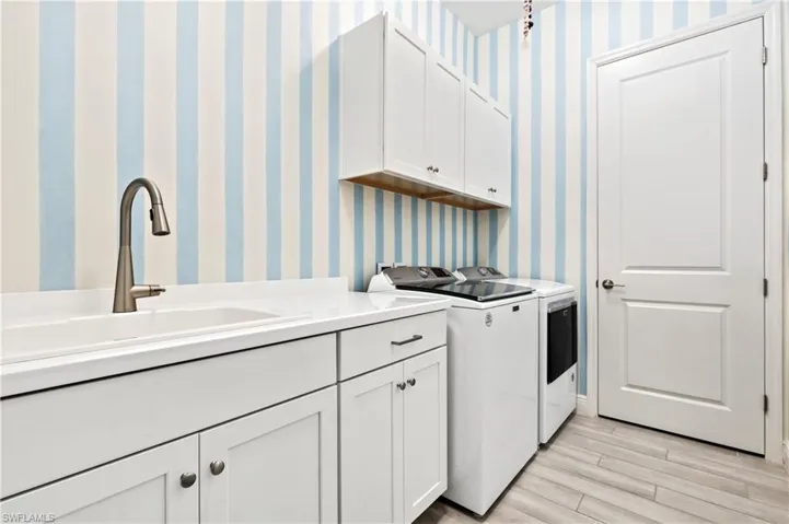 Laundry room featuring cabinet space, separate washer and dryer, light wood finished floors, and wallpapered walls