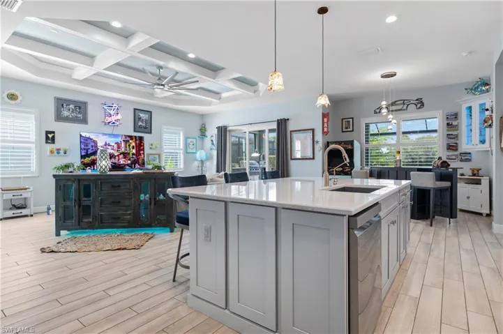 Kitchen with light stone counters, gray cabinetry, a kitchen bar, a kitchen island with sink, and coffered ceiling