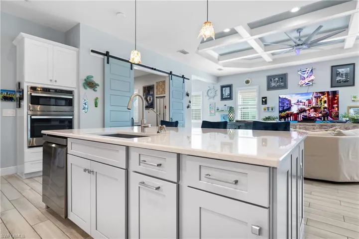 Kitchen featuring a barn door, open floor plan, wood tiled floors, white cabinets, and coffered ceiling
