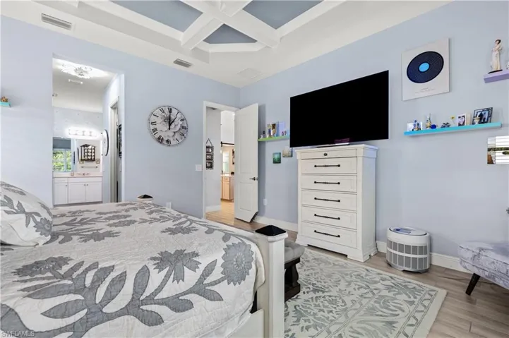 Bedroom featuring coffered ceiling, light wood-type flooring, and ensuite bath