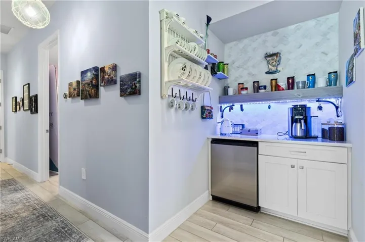 Indoor wet bar featuring open shelves, stainless steel refrigerator, white cabinets, tasteful backsplash, and light wood-type flooring