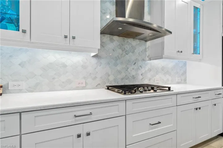 Kitchen with white cabinets, light stone countertops, glass insert cabinets, tasteful backsplash, and stainless steel gas stovetop