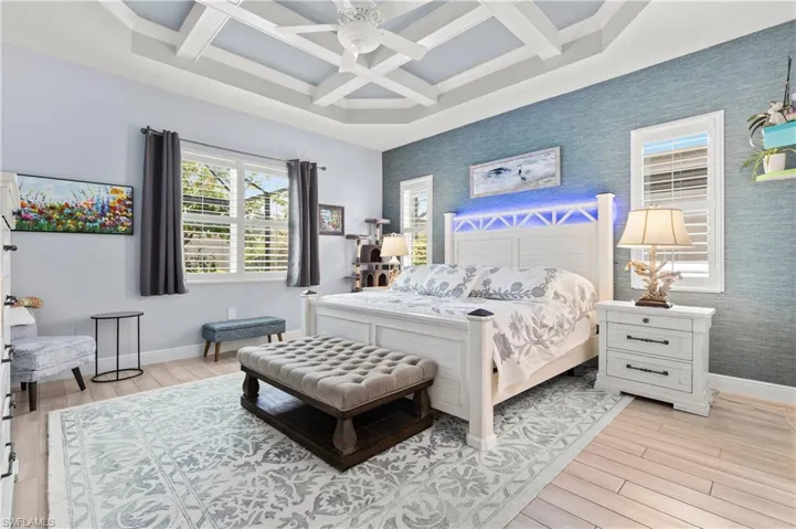 Bedroom with wallpapered walls, coffered ceiling, light wood-type flooring, a ceiling fan, and an accent wall