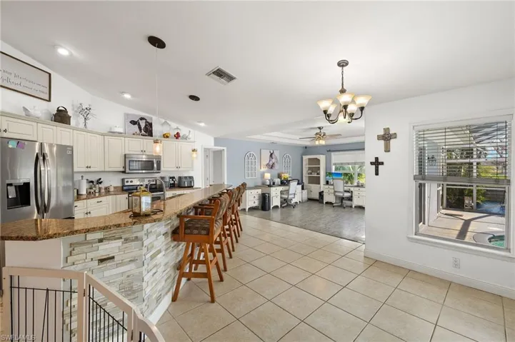 Kitchen featuring ceiling fan with notable chandelier, dark stone counters, stainless steel appliances, light tile patterned floors, and visible vents