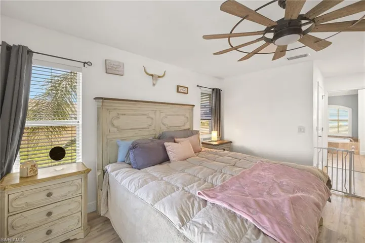 Bedroom with multiple windows, light wood-type flooring, ceiling fan, and visible vents