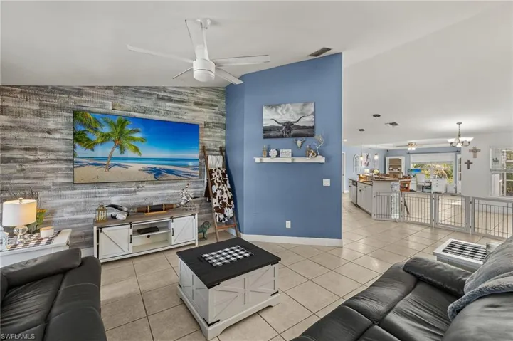 Living room with an accent wall, ceiling fan with notable chandelier, baseboards, light tile patterned floors, and visible vents