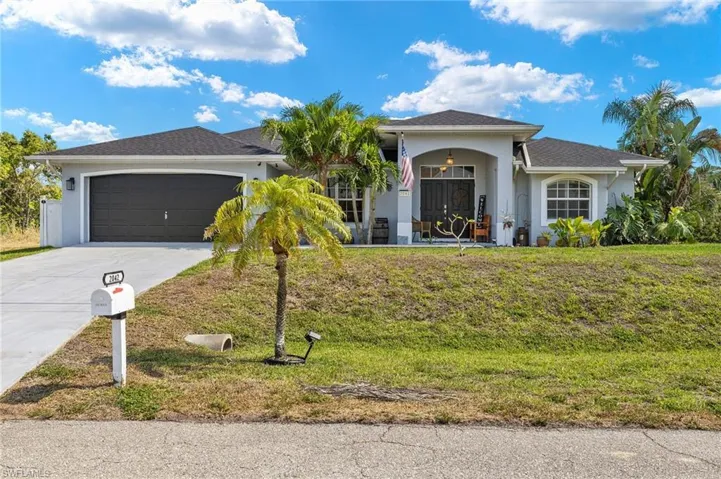 View of front facade featuring an attached garage, driveway, stucco siding, and a front yard