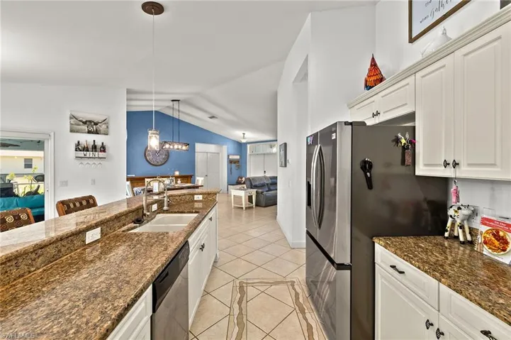 Kitchen with lofted ceiling, light tile patterned flooring, a sink, appliances with stainless steel finishes, and decorative light fixtures
