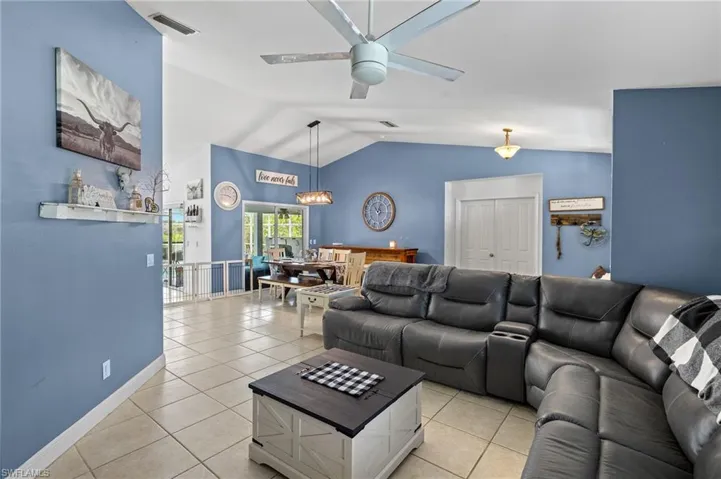 Living area featuring light tile patterned flooring, ceiling fan, baseboards, lofted ceiling, and visible vents