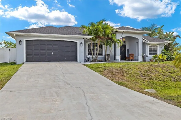 Ranch-style home with covered porch, driveway, a front yard, a garage, and stucco siding