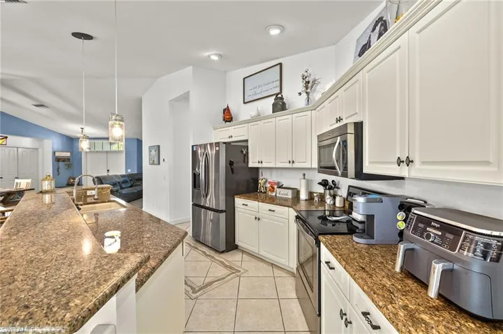 Kitchen featuring a sink, stainless steel appliances, decorative light fixtures, light tile patterned floors, and vaulted ceiling