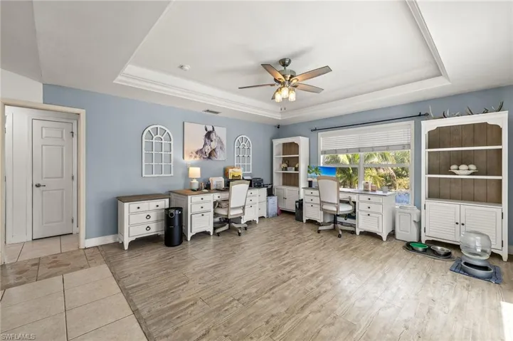 Office area featuring a ceiling fan, baseboards, wood finished floors, a tray ceiling, and visible vents
