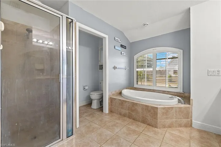 Bathroom featuring a garden tub, a stall shower, tile patterned floors, toilet, and lofted ceiling