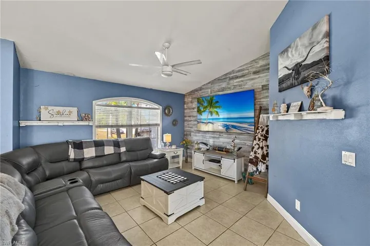 Tiled living room featuring baseboards, ceiling fan, an accent wall, and lofted ceiling