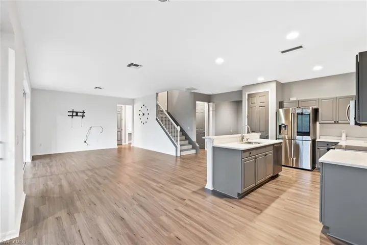 Kitchen featuring gray cabinetry, appliances with stainless steel finishes, a kitchen island with sink, light wood finished floors, and recessed lighting