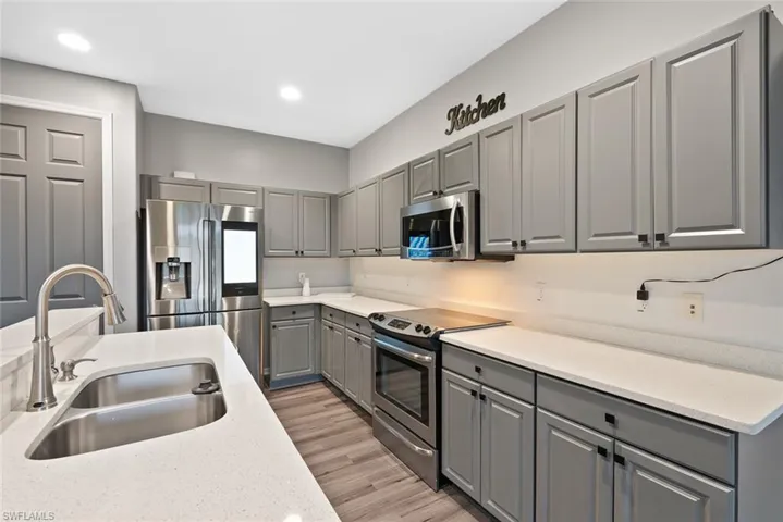 Kitchen with appliances with stainless steel finishes, gray cabinets, a sink, light wood finished floors, and light countertops