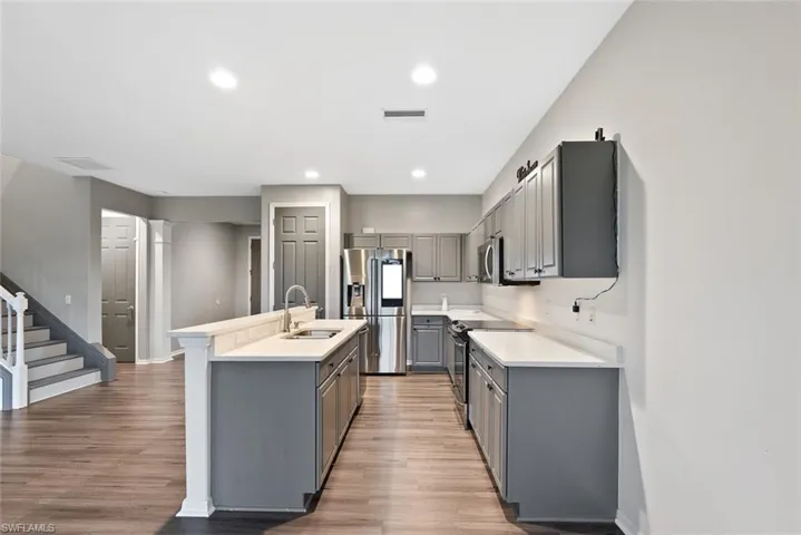 Kitchen with gray cabinetry, appliances with stainless steel finishes, a sink, a kitchen island with sink, and light wood-style flooring