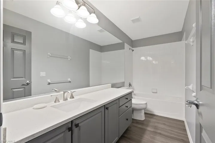 Bathroom with vanity, toilet, wood finished floors, tub / shower combination, and a chandelier