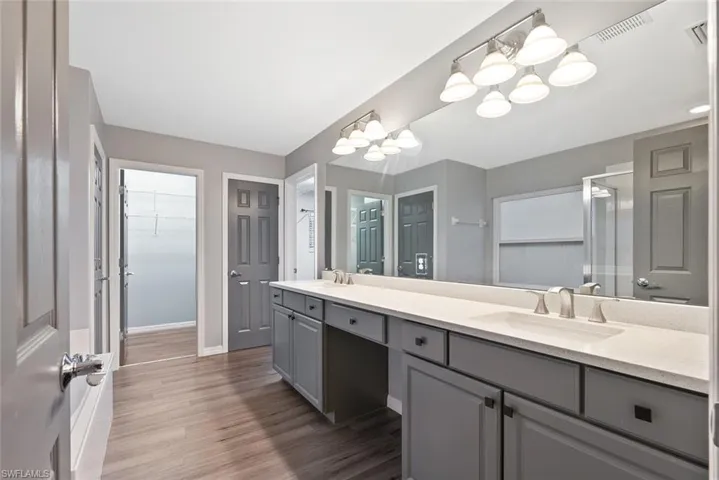 Full bath featuring a chandelier, double vanity, baseboards, wood finished floors, and a walk in closet