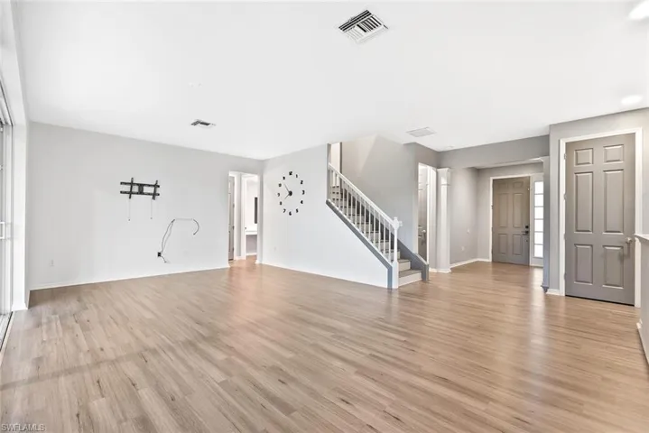 Unfurnished living room with stairway, light wood-style floors, and baseboards