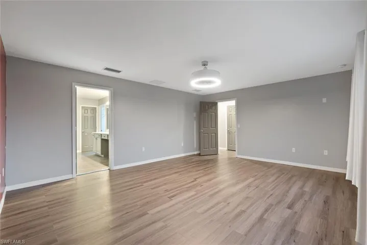 Unfurnished bedroom with light wood-style flooring, baseboards, and ensuite bath
