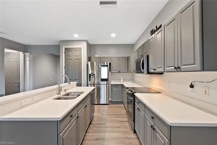 Kitchen featuring gray cabinets, appliances with stainless steel finishes, a sink, light wood-style floors, and recessed lighting