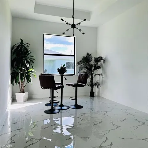 This space features sleek, glossy tiled flooring with a marble-like pattern, a large window providing natural light, and a modern black sputnik-style chandelier