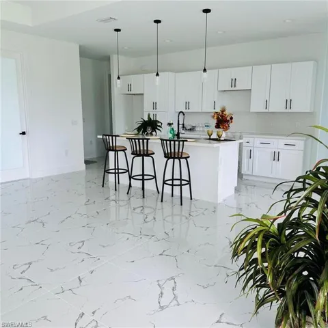 The kitchen features white cabinetry, a kitchen island with seating for three, and pendant lighting
