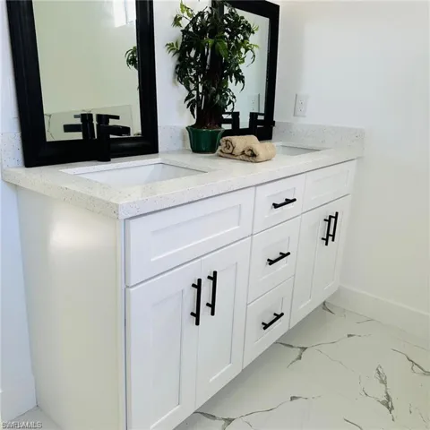 Contemporary bathroom vanity with dual sinks, white cabinetry, speckled countertops, and black hardware