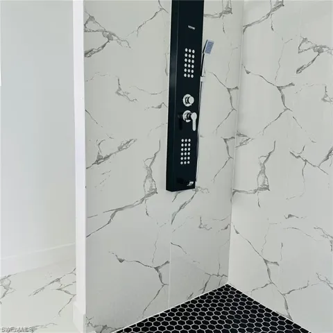 Shower featuring a black shower panel with integrated controls and handheld showerhead, white and grey marble-effect wall tiling, and black hexagonal floor tiling