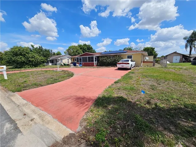 Single story home with concrete driveway, solar panels, and a front lawn
