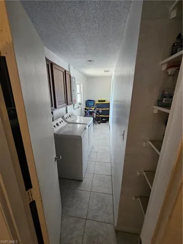 Laundry room featuring a textured ceiling, light tile patterned floors, washer and clothes dryer, and cabinet space