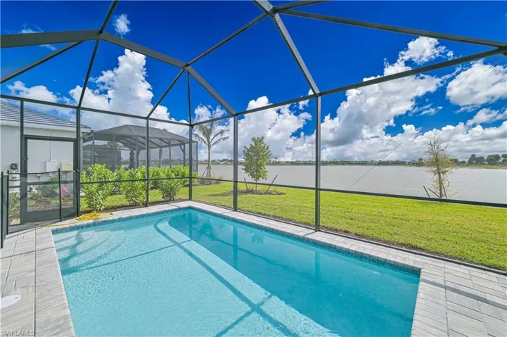 Outdoor pool with glass enclosure, a lawn, a sunroom, and a water view