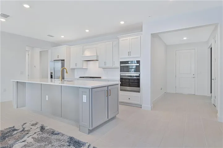 Kitchen featuring white cabinets, recessed lighting, gray cabinetry, appliances with stainless steel finishes, and custom range hood