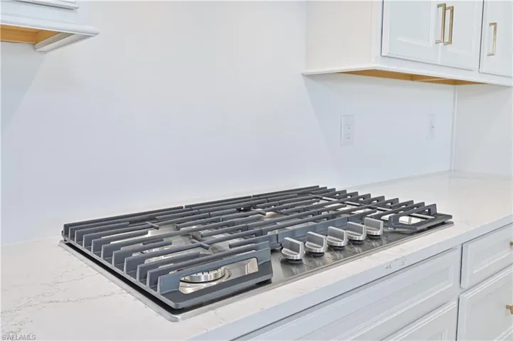 Kitchen view of stainless steel gas stovetop, white cabinetry, and light stone countertops
